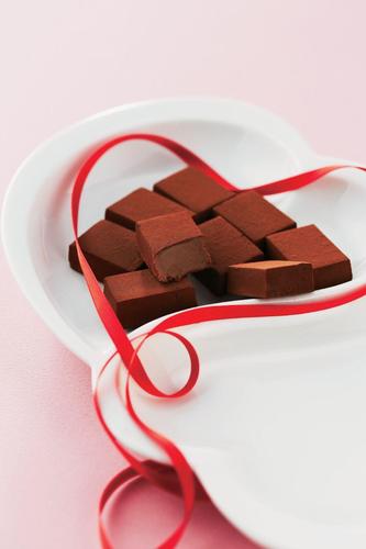 White heart-shaped dish with cocoa-dusted chocolate truffles, accented by a red ribbon for a festive, Valentine's Day presentation.