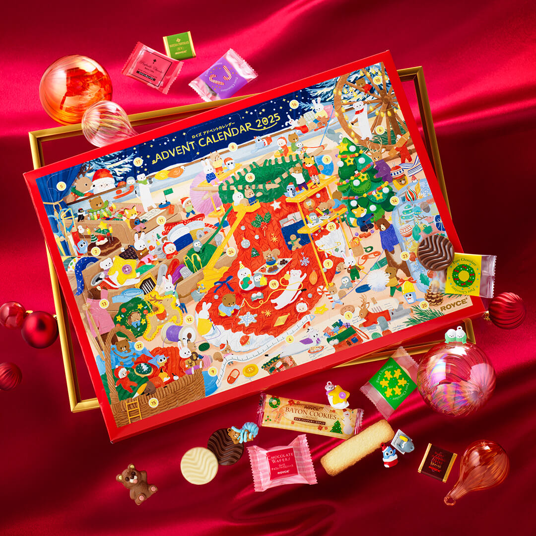Festive 2025 Advent calendar with forest-animal illustration, surrounded by assorted Royce chocolates, cookies, ornaments, and holiday-shaped candies on red satin cloth.