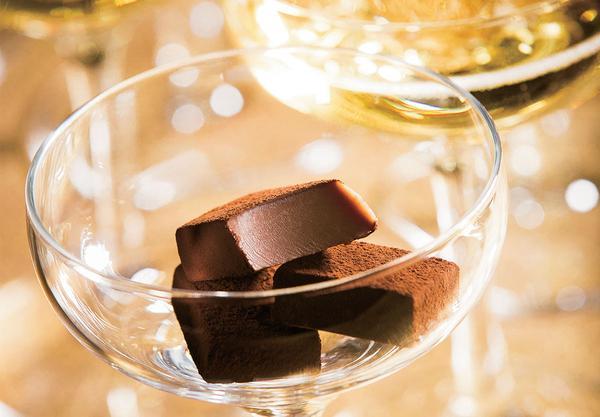 Small chocolate Nama pieces, coated with cocoa powder, displayed in a clear stemmed glass, suggesting an elegant dessert or after-dinner setting.