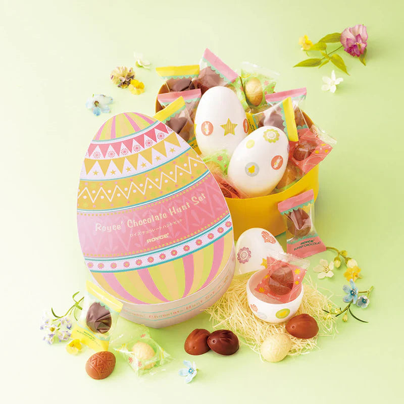 Easter-themed chocolate gift set with a pastel-striped egg box, plastic eggs, wrapped chocolates, colorful packets, and decorative faux flowers on straw.