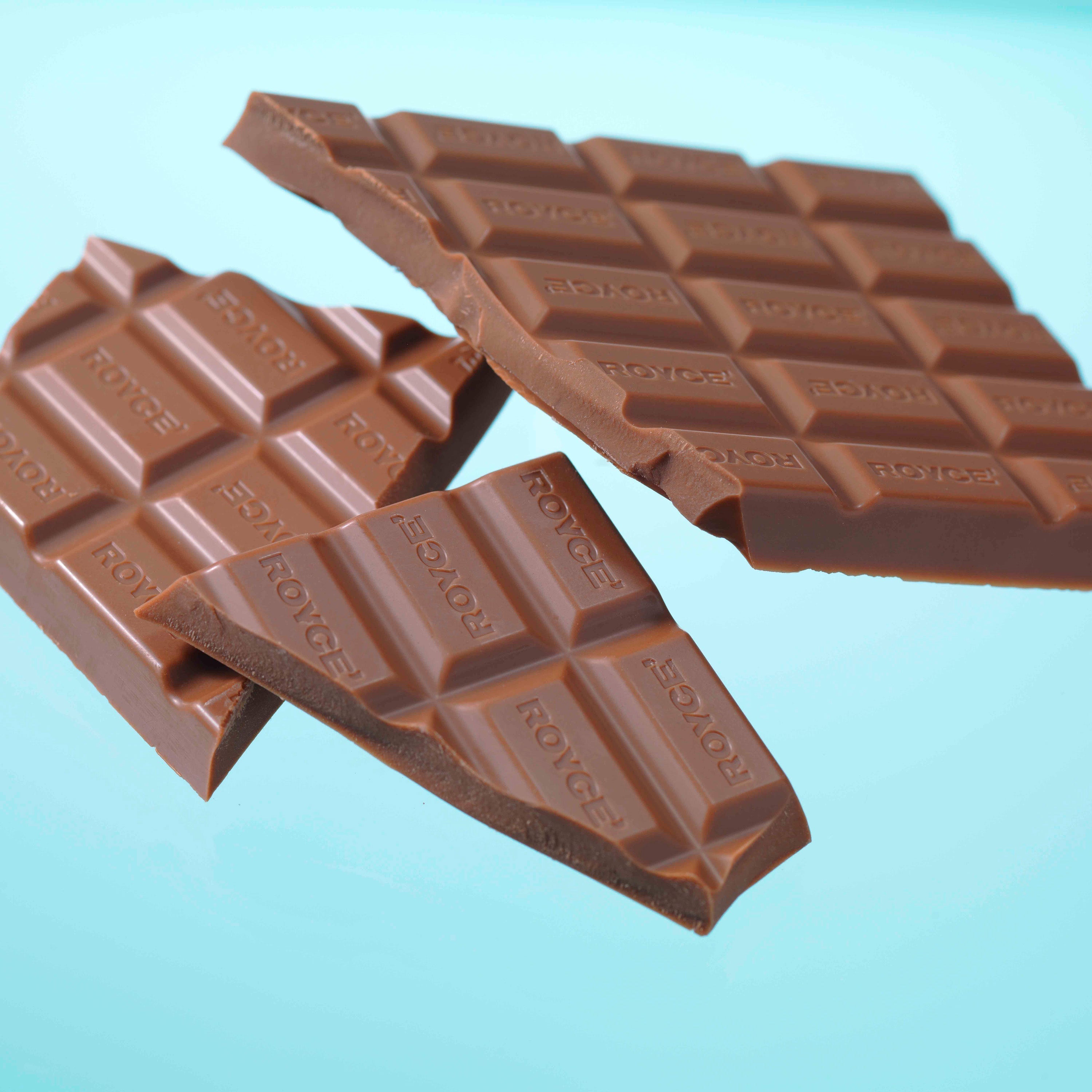 Segments of a Royce milk chocolate bar with visible ROYCE branding floating in an artistic arrangement.