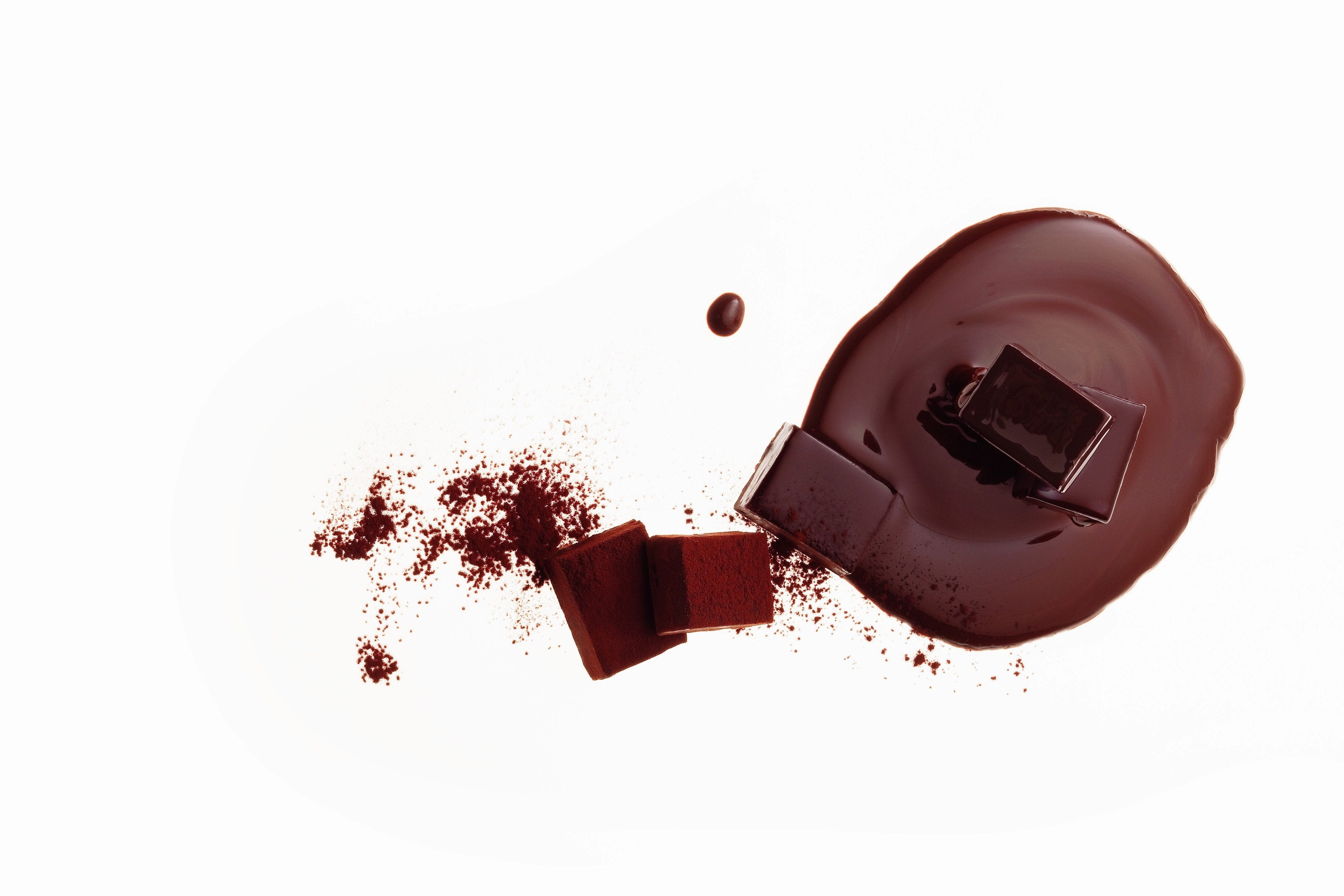 Assorted dark chocolates with solid Namas on melted chocolate, cocoa-dusted cubes, and a mid-air chocolate droplet, showcasing rich chocolate textures.