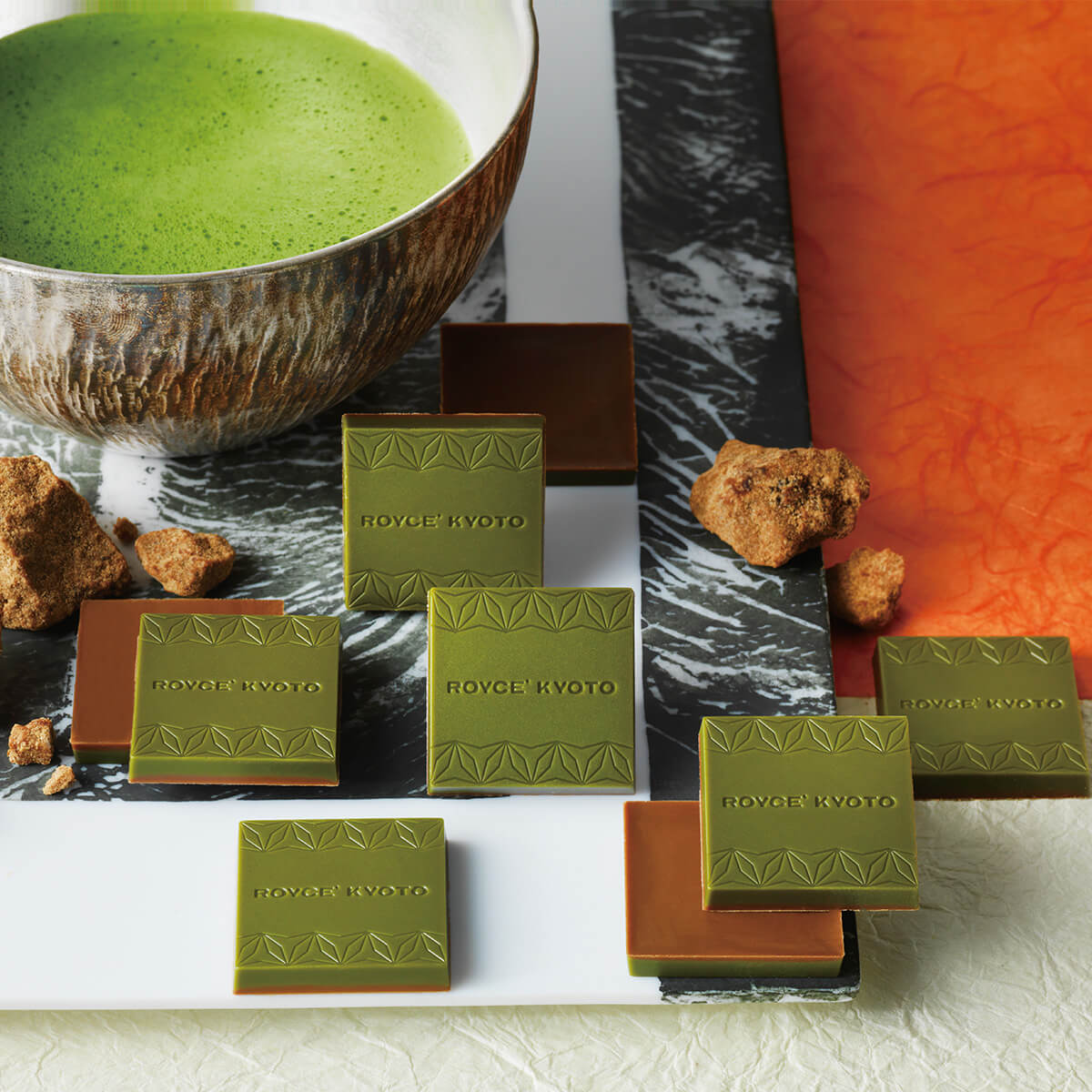 Matcha chocolates from ROYCE’ KYOTO on marble; embossed green tops, brown bases, with frothy matcha tea and kinako scattered around.