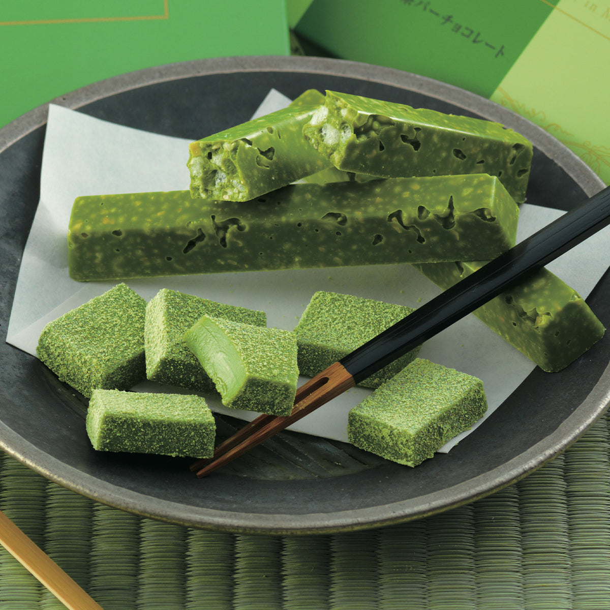 Assortment of matcha chocolates: aerated bars and powder-coated Namas on a plate, served with chopsticks on a traditional mat.