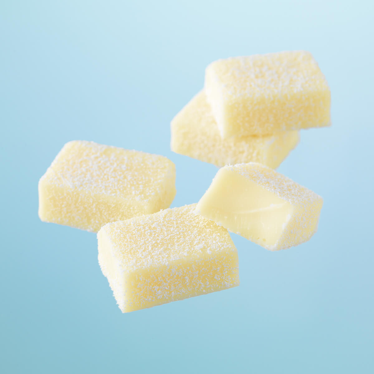 Five white, dusted Namas, one cut open to show a jelly-like interior, resembling fruit jellies or gummy candies.