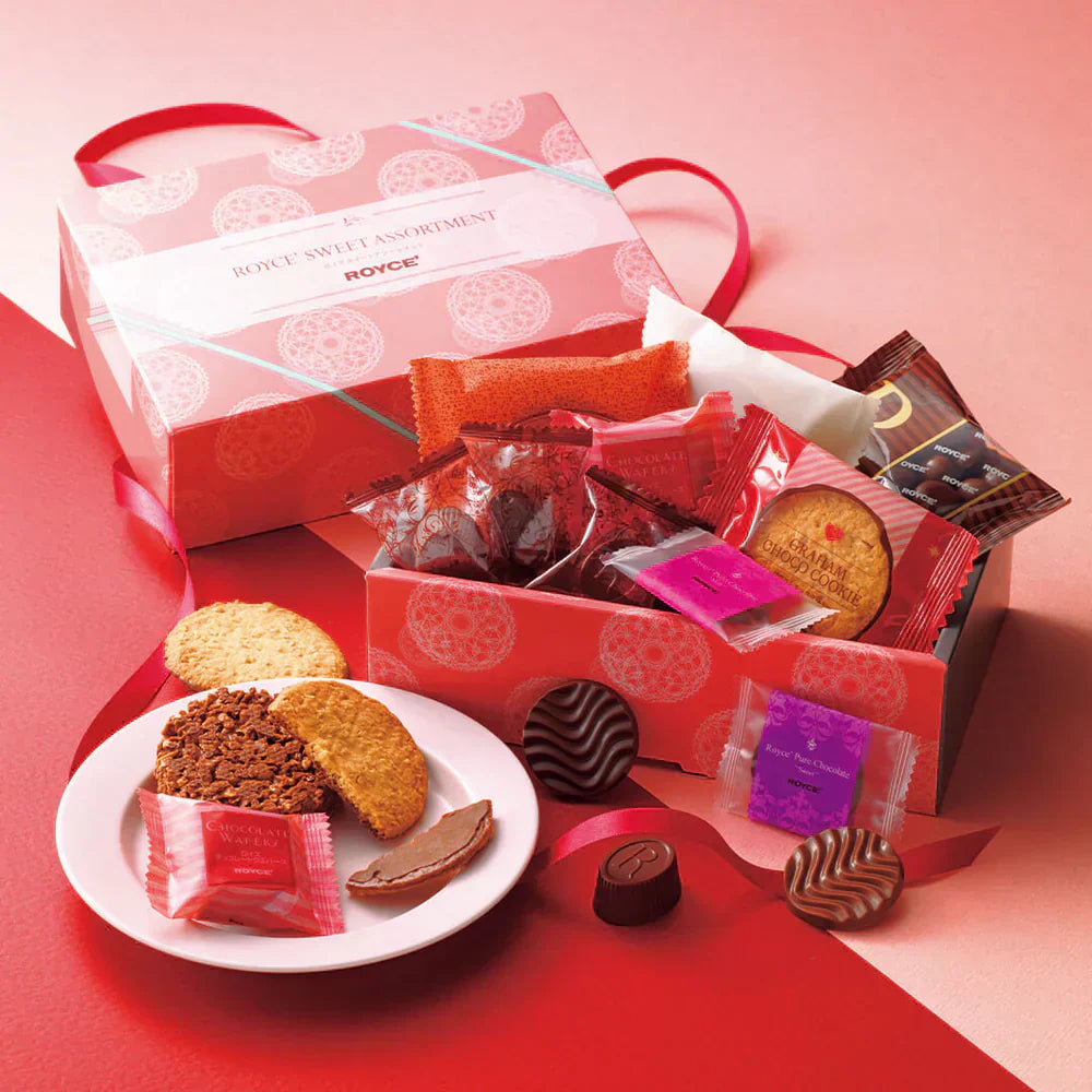 Pink ROYCE' SWEET ASSORTMENT box with ribbon handle, featuring chocolate-coated wafers, graham cookies, praline chocolates, and a partially eaten cookie on a plate.