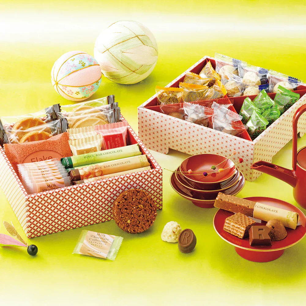 Decorative gift boxes with assorted wrapped confections, red lacquer teapot, matching dishes, and embroidered temari balls.