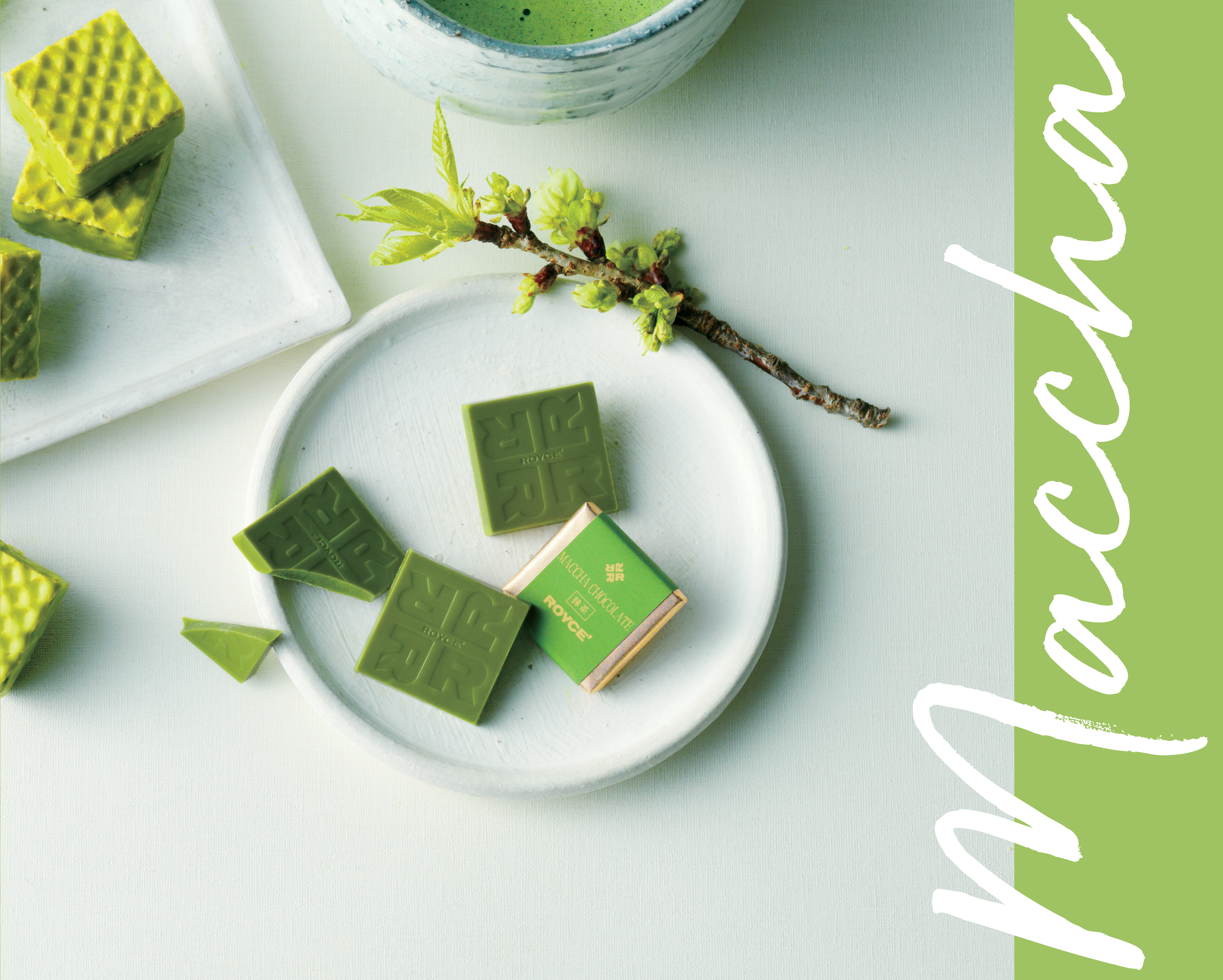 Flat-lay of matcha-green sweets: ROYCE chocolate squares, matcha wafer sandwiches, frothy matcha tea in a bowl, and decorative twig with green blossoms.