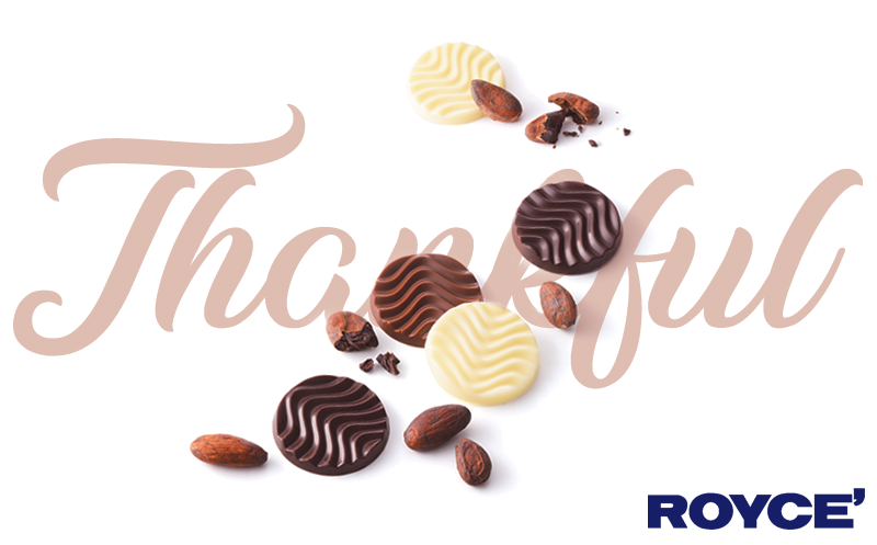 Five round ROYCE’ Pure. chocolates in dark, milk, and white varieties, surrounded by cocoa beans and nibs, with a faint Thankful script and ROYCE’ logo.