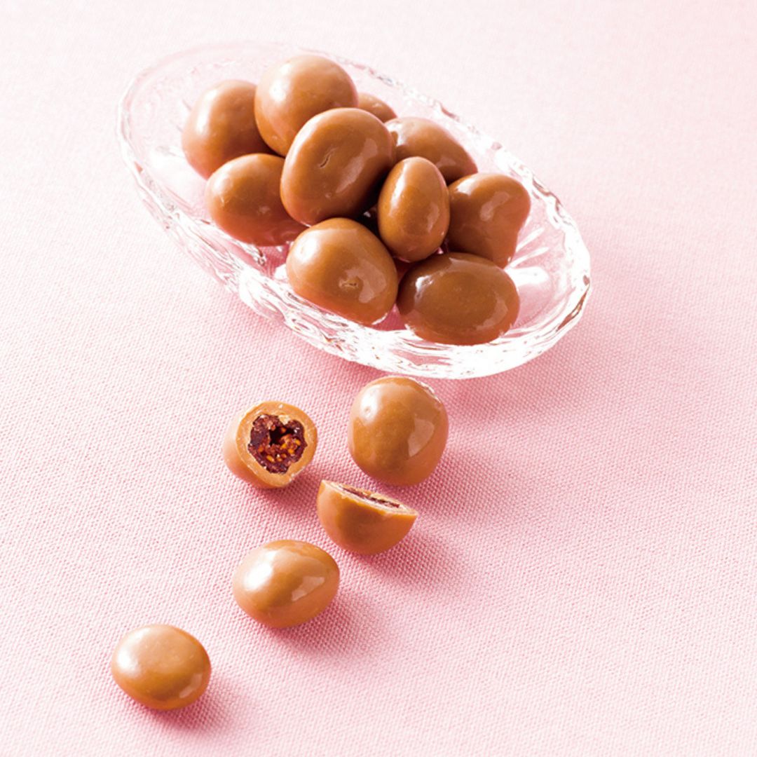Glass dish with glossy milk-chocolate-coated berries, some cut open to reveal dried fruit centers, typically cranberries, on a simple background.