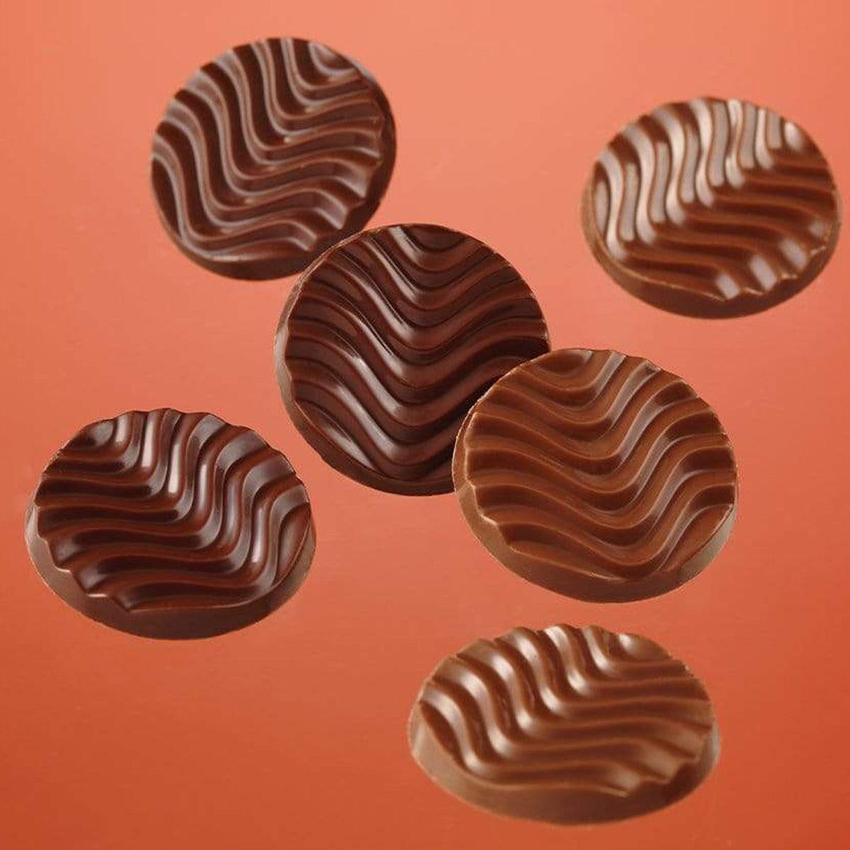Floating Pure chocolate discs with a wavy-line pattern, resembling sculpted medallions, showcasing their milk and dark chocolate craftsmanship.
