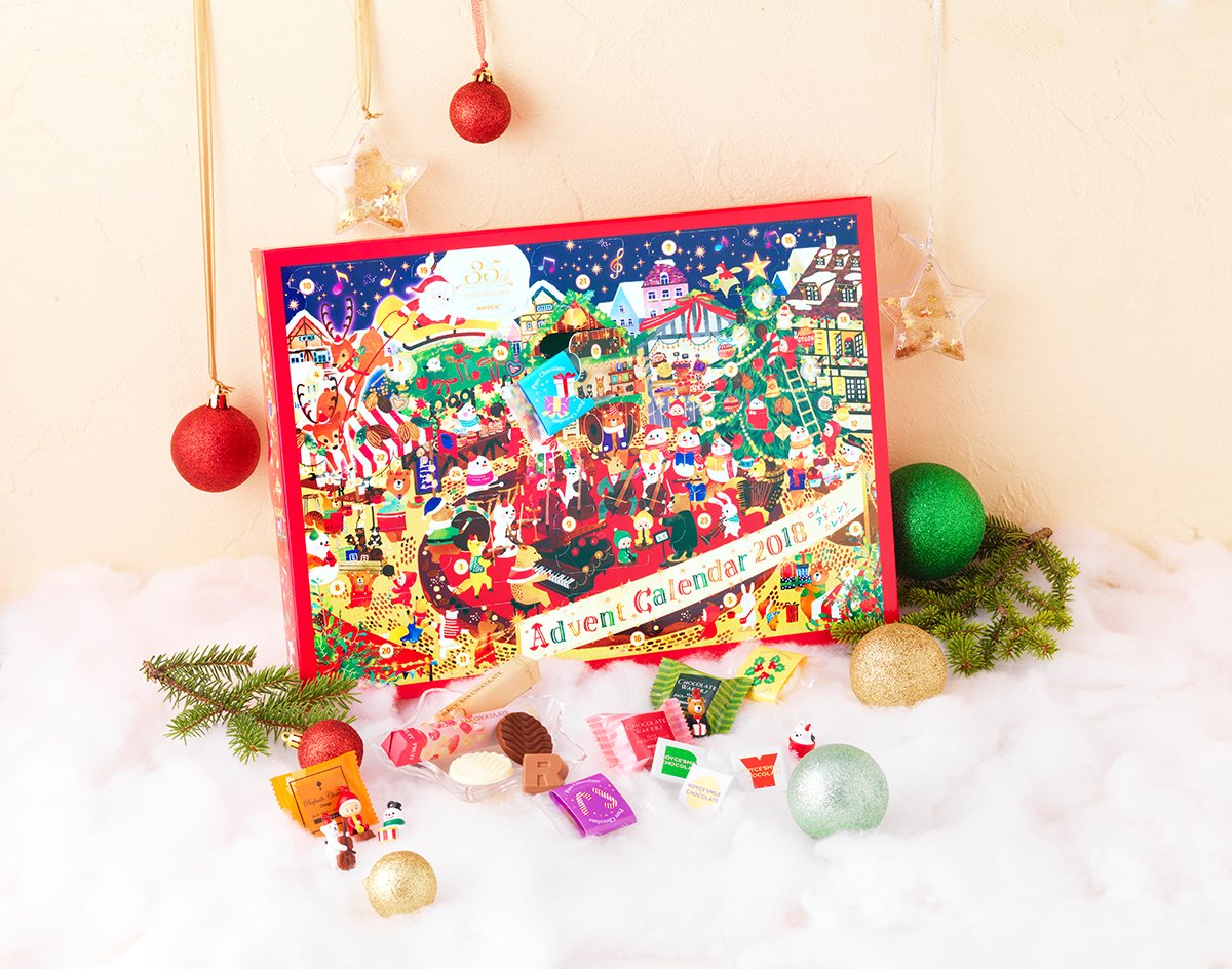 Festive holiday display featuring a colorful Advent Calendar 2018 with Santa, reindeer, and nutcrackers, surrounded by ornaments, chocolates, and evergreen sprigs.