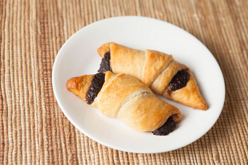 Two golden-brown crescent pastries with Nama chocolate filling on a white plate, placed on a woven placemat.