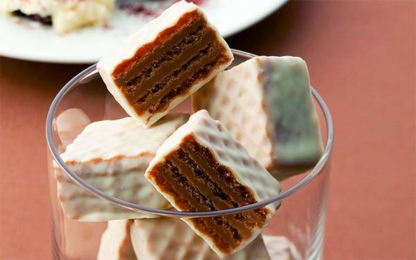 Close-up of square wafer cookies with layers of crispy wafers and chocolate filling, coated in white chocolate, piled in a clear glass.