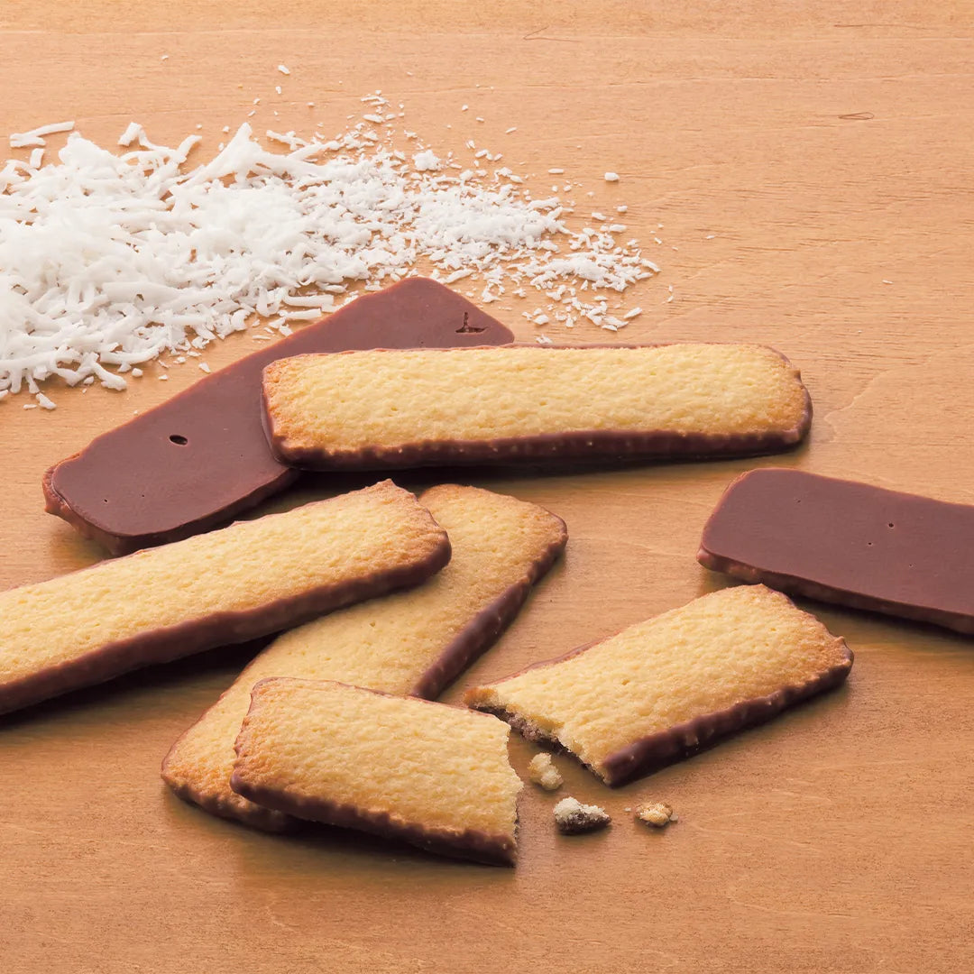 A small pile of golden-brown shortbread cookies with chocolate-dipped edges, surrounded by shredded coconut, one cookie broken in half with crumbs.