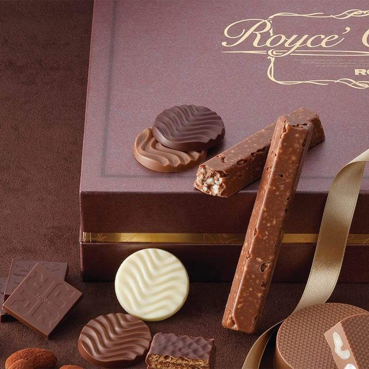 Assorted chocolates on a decorative gift box: milk-chocolate sticks, round coins, embossed squares, cut wafer piece, and loose almonds.