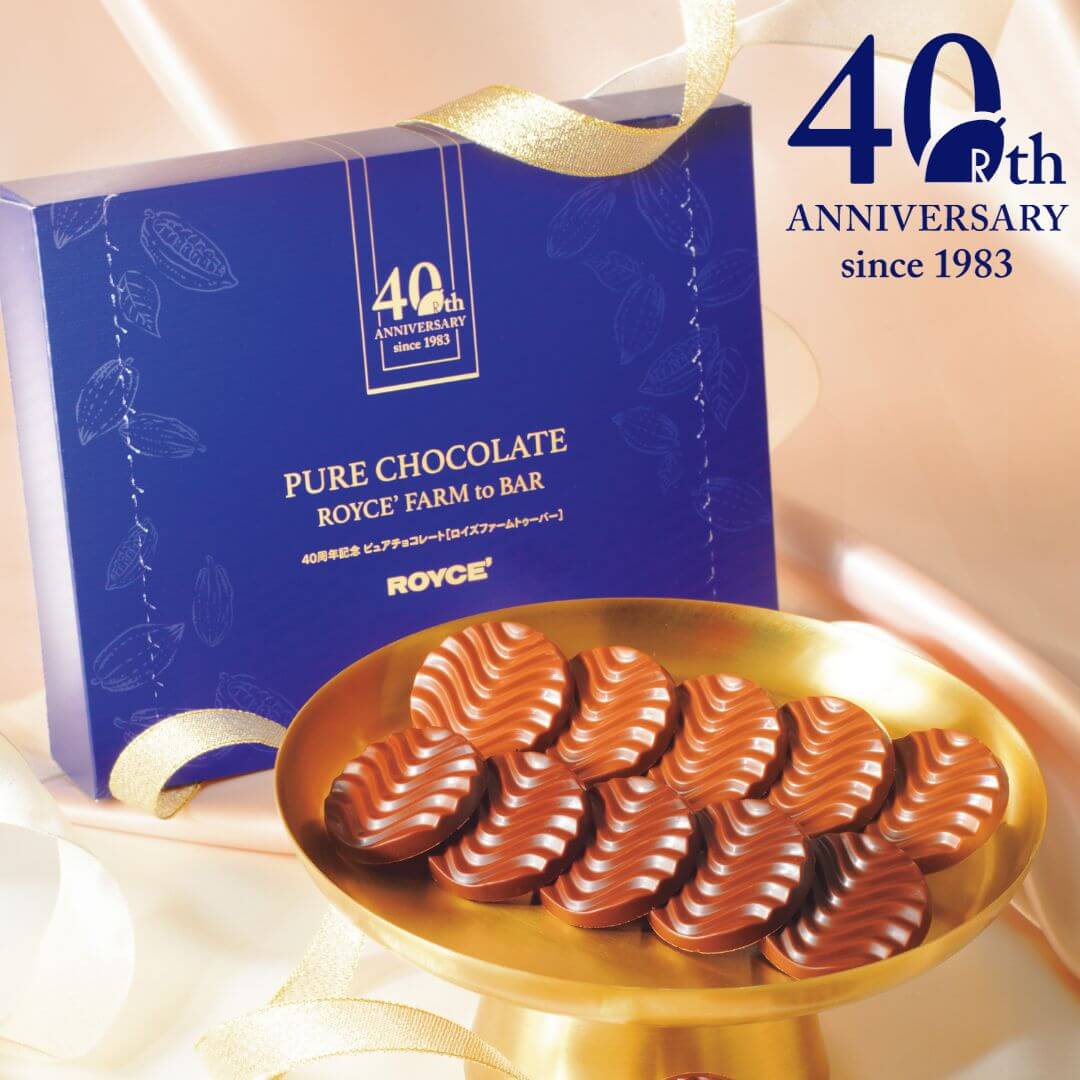 Image shows a blue box with a gold plate and brown chocolate discs. Text says 40th Anniversary since 1983. 40th Pure Chocolate ROYCE' Farm to Bar. ROYCE'.