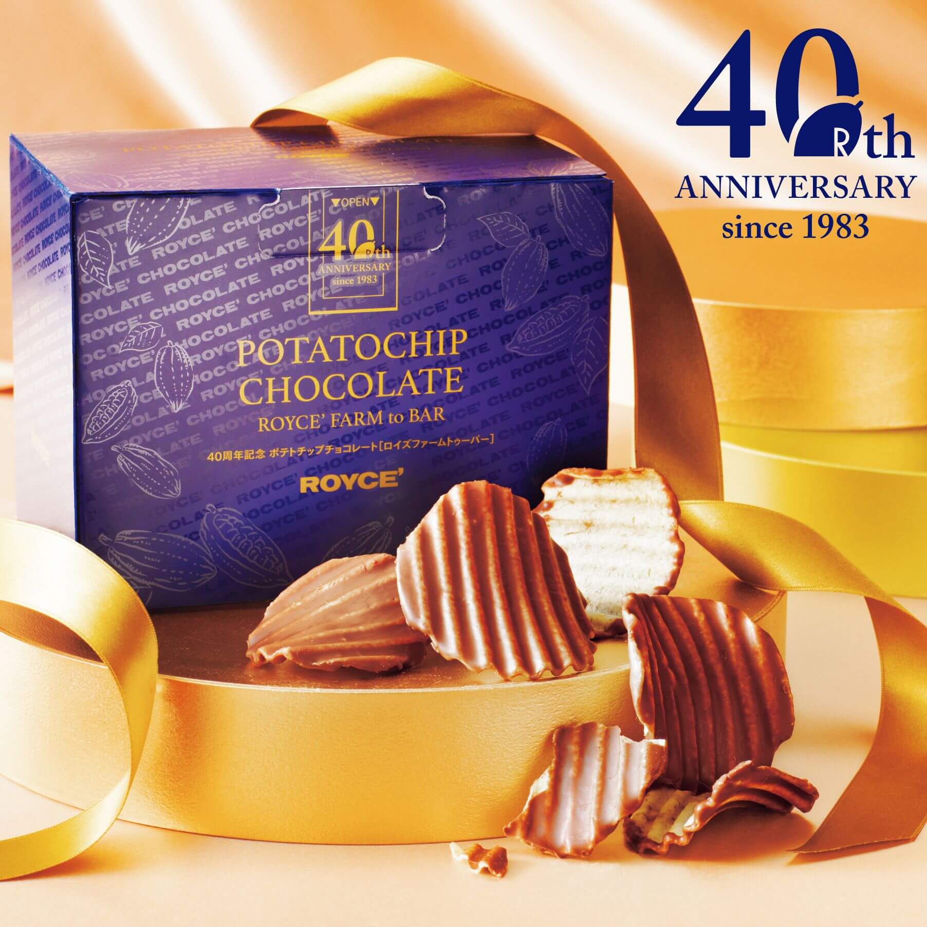 ROYCE' Chocolate - 40th Anniversary Potatochip Chocolate "ROYCE' Farm To Bar" - Image shows a blue printed box with gold text saying 40th Anniversary since 1983 Potatochip Chocolate ROYCE' Farm to Bar ROYCE'. Blue text on upper right says 40th Anniversary Since 1983. Image as a whole also has gold ribbons and platforms together with loose brown-colored chocolate-coated potato chips.