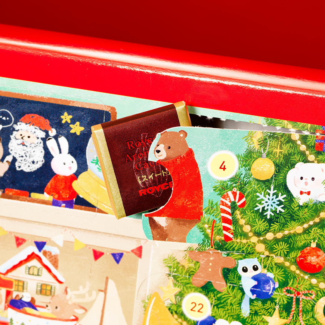 A close-up of a red box or tray containing colorful illustrated advent-style cards or envelopes. One card is partially pulled open, showing a brown bear illustration with the word ROYCE' and gold trim.