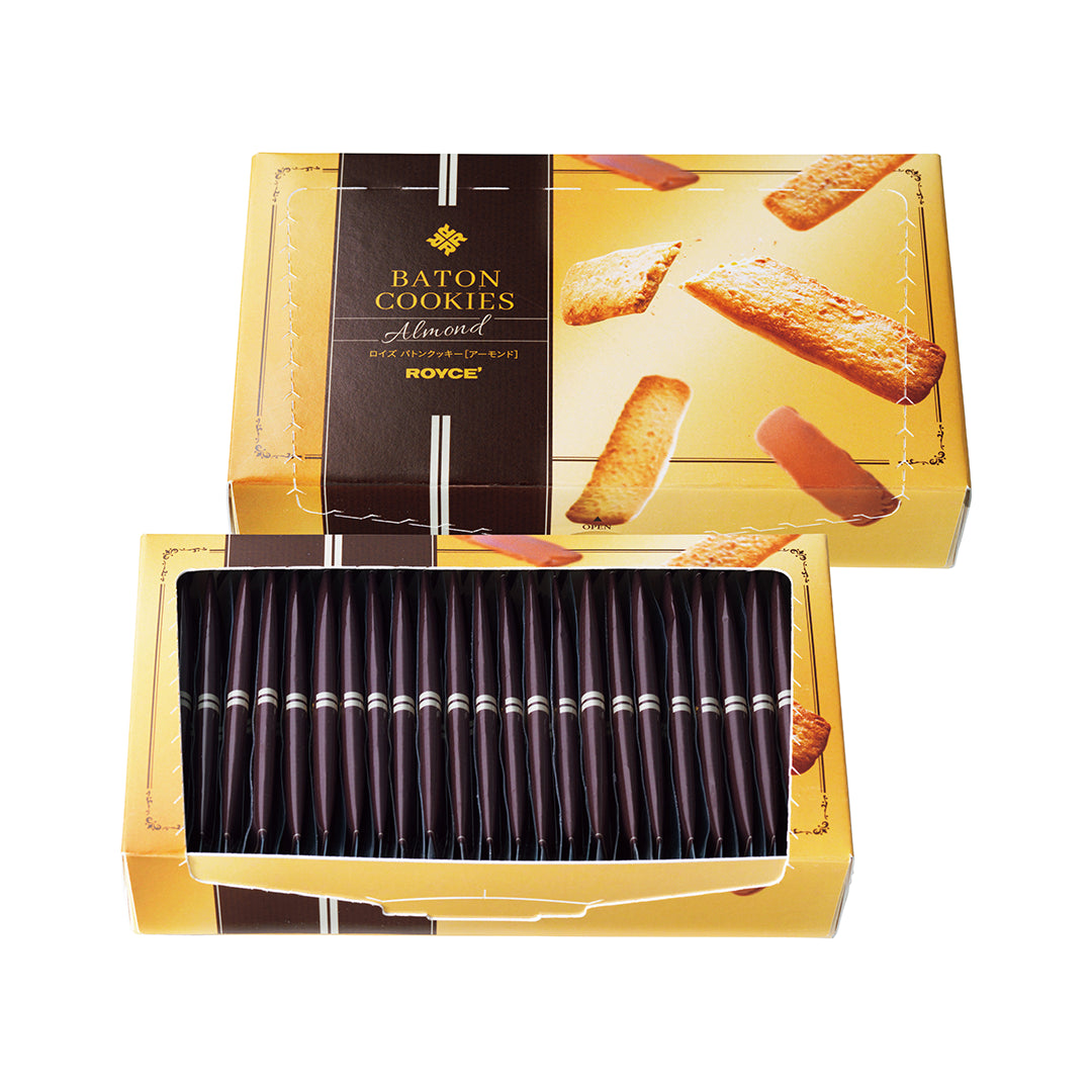 Baton Cookies "Almond" - A rectangular box of ROYCE' Baton Cookies, Almond flavor, shown on a plain white background. The packaging is gold with a dark brown vertical detail on the left with text saying Baton Cookies Almond ROYCE'. Image also shows a gold box on the bottom with individually-wrapped cookies.
