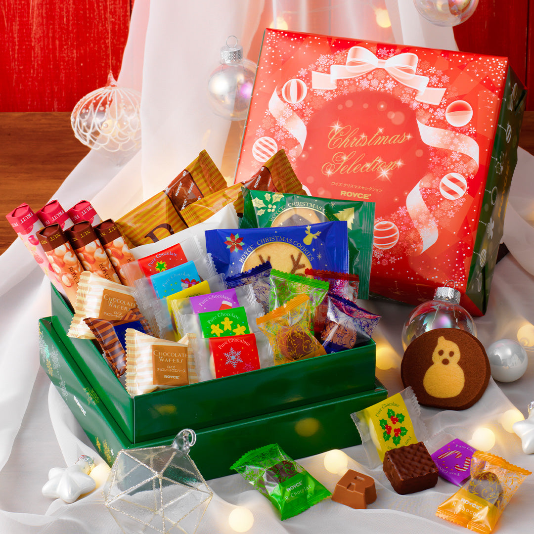 Image shows green and red boxes with individually-wrapped chocolates. Red box has illustrations of snowflakes, balls, and ribbons and has text saying Christmas Selection ROYCE'.