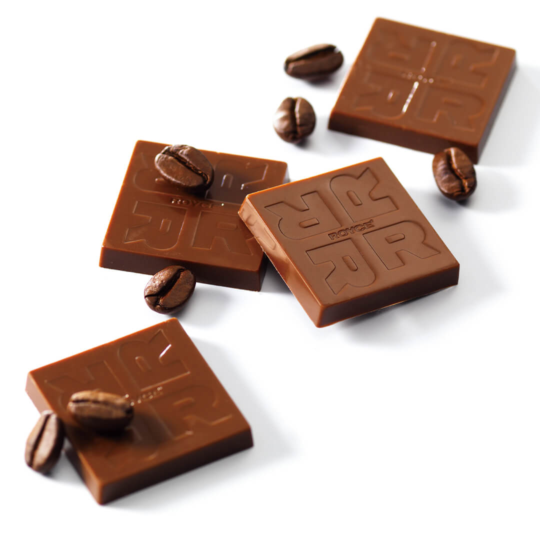 ROYCE' Chocolate - Coffee Chocolate - Image shows brown chocolate squares embossed with the letter R and word ROYCE'. Also included in the picture are loose coffee beans.