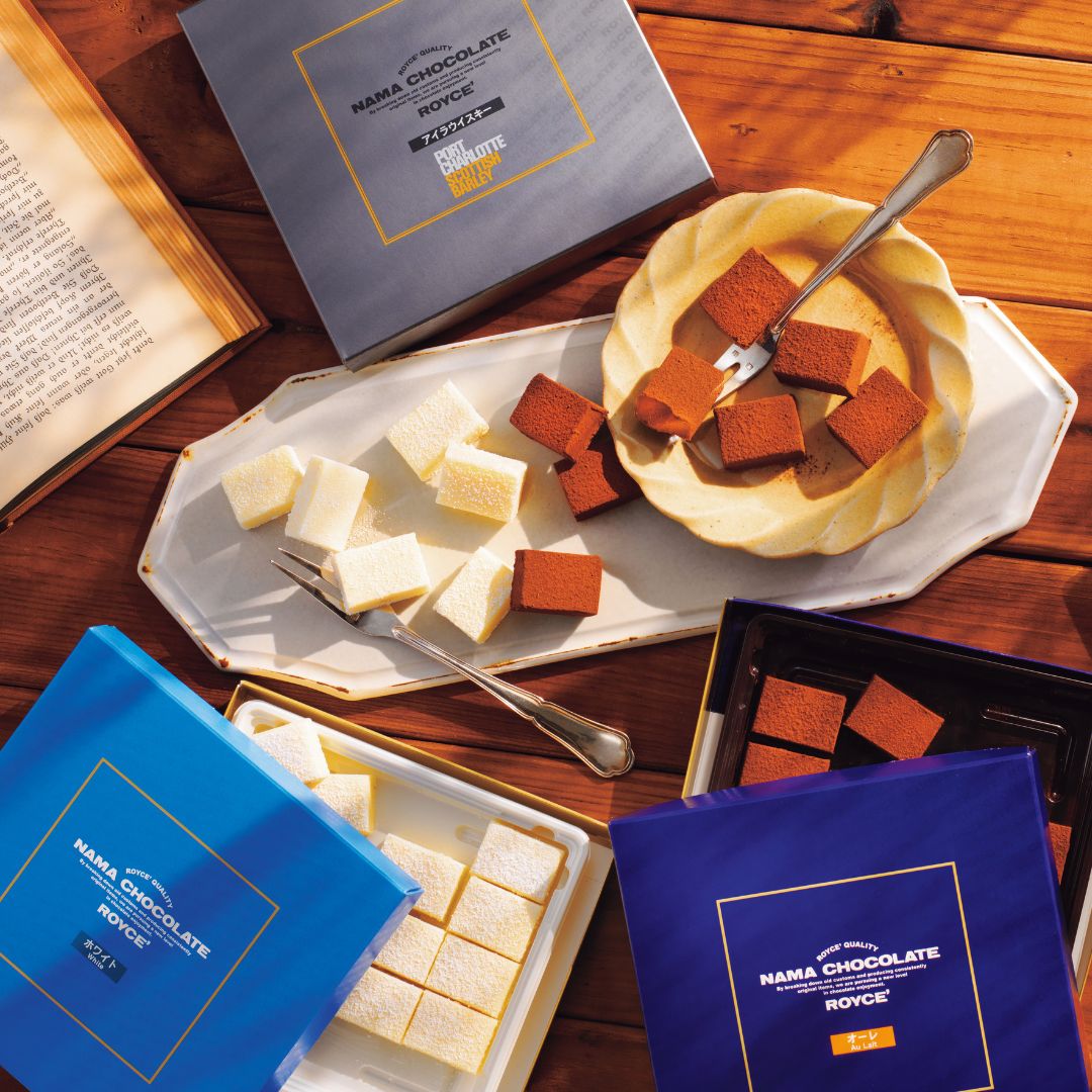 Image shows white and brown chocolates on a trays and plates together with boxes on a wooden surface.