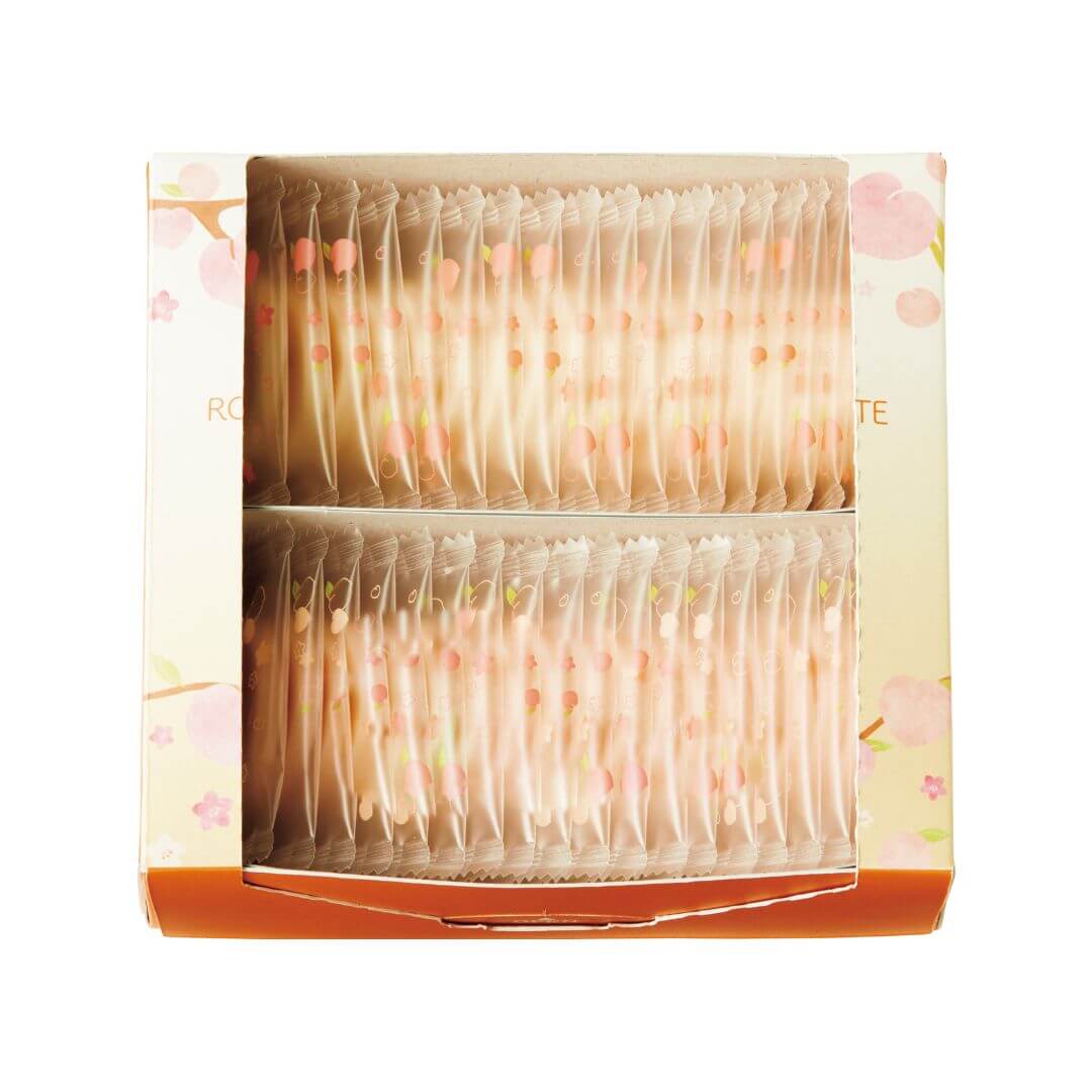 ROYCE' Chocolate - Hakutouberry & Hakutouwhite Chocolate - Image shows an open box in the colors of peach and orange with illustrations of peaches, flowers, twigs, and leaves on each side. Inside of the box shows individually-wrapped chocolate discs in white (inset above) and light pink (inset below). Chocolates' wrappers are transparent with prints of peaches and flowers in pink and green.
