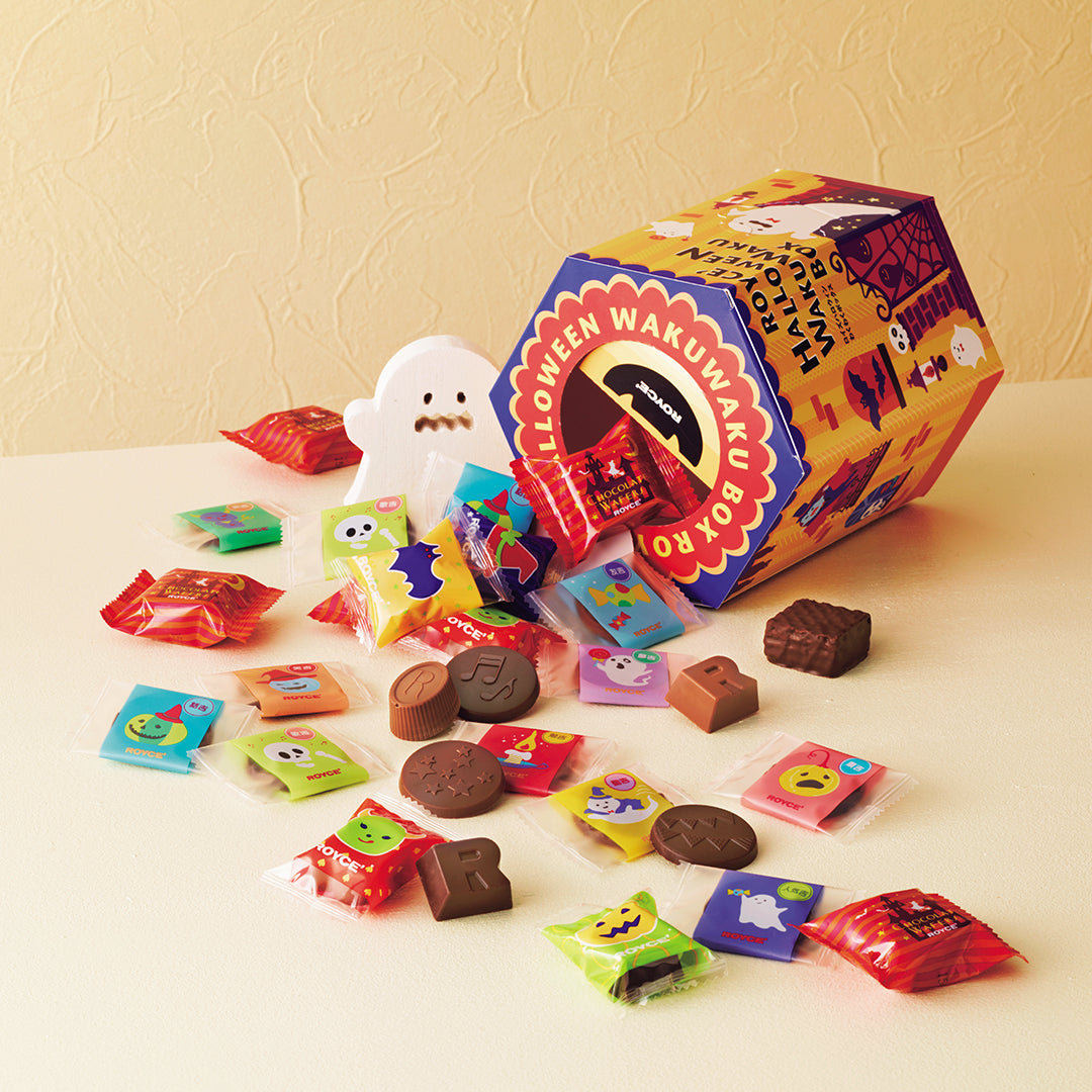 ROYCE' Halloween Wakuwaku Box - A colorful Halloween-themed candy box labeled 'Halloween Wakumaku Box' tipped over with assorted wrapped candies and chocolate pieces spilled onto a light cream surface against a textured beige wall.