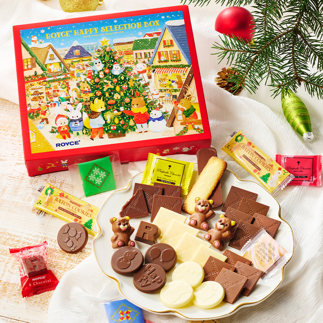 A festive Christmas-themed cookie box set by Royce, shown with its illustrated red gift box and an assortment of decorated cookies on a white plate. The cookies include chocolate and white chocolate pieces shaped like bears, letters, and ornaments, alongside small wrapped candies.