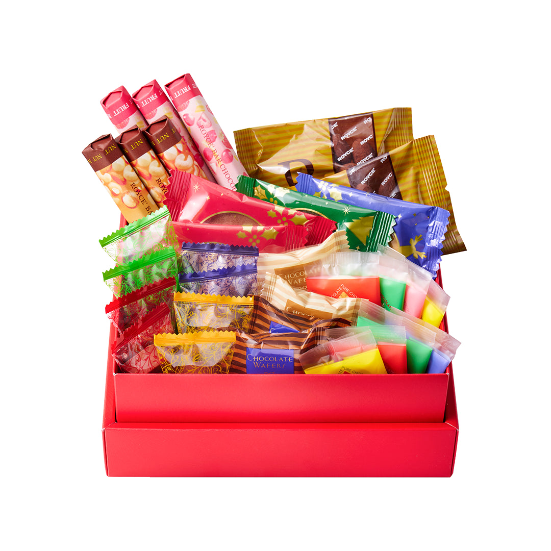 A red gift box filled with assorted packaged snacks, candies, and stick packs, photographed on a clean white background.