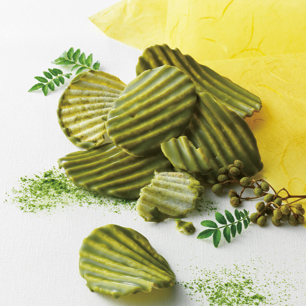 ROYCE' Kyoto Potatochip Chocolate "Uji Matcha & Sansho" - Image shows potato chips coated in green chocolate. Accents include matcha powder dustings, green leaves, grape-shaped peppers, and a yellow paper.