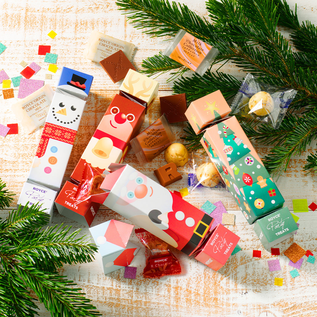 Image shows printed cylinders with accents of loose chocolates, leaves, and paper cutouts on a wooden white surface.