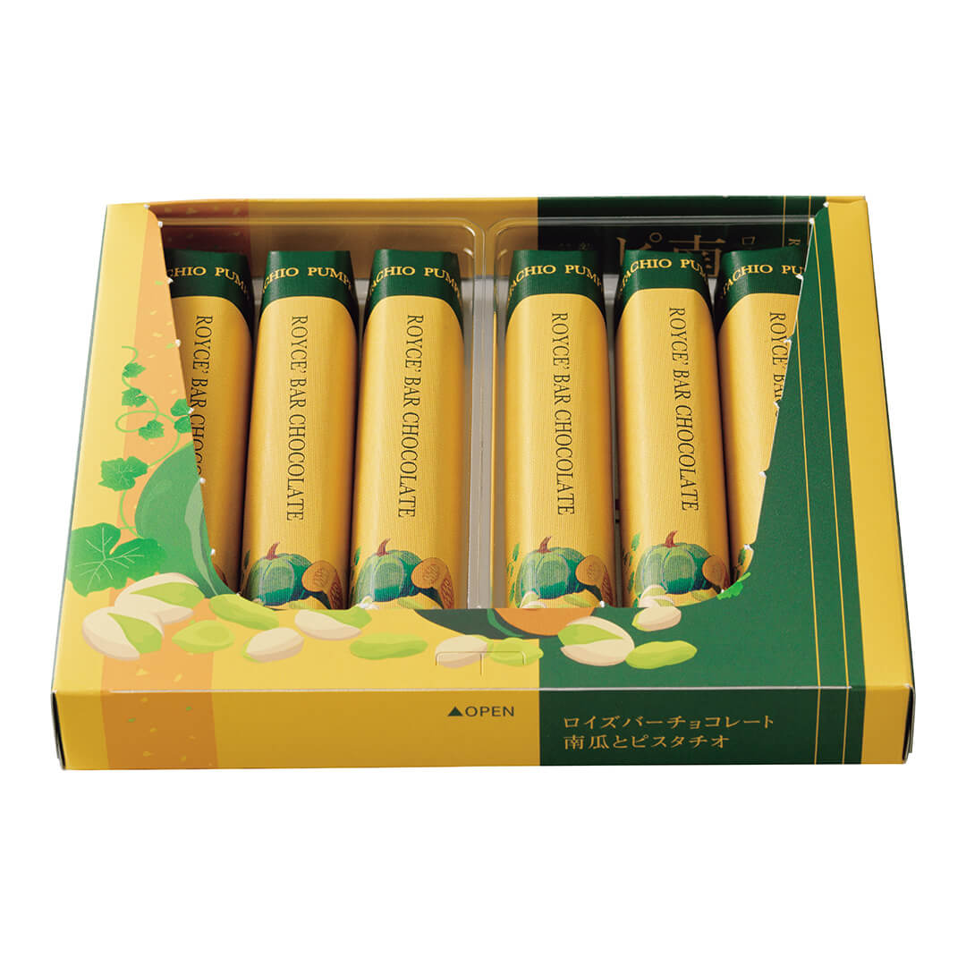 Image shows a printed open box in the colors of yellow and green., with illustrations of loose pistachio nuts in green and light yellow as well as a pumpkin with leaves in green. Inside the box are finger-shaped bar confections with wrapper in the colors of yellow and green with illustrations of pumpkins in green and yellow below. Text from middle top says Pistachio Pumpkin. ROYCE' Bar Chocolate. Green text on bottom center says Open with a green upward arrow on the left. Background is in white.