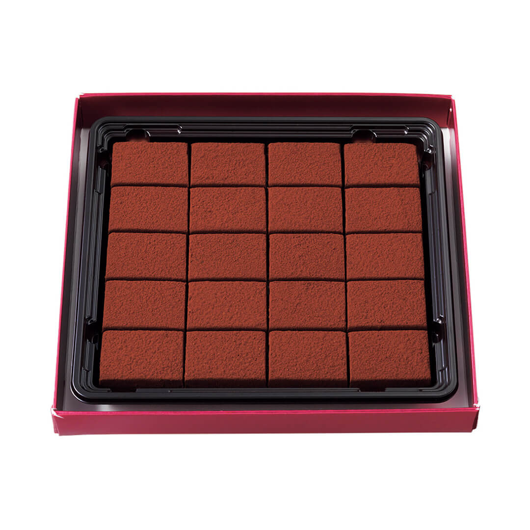 Image shows a red box with a black tray containing brown chocolate blocks. Background is in color white.