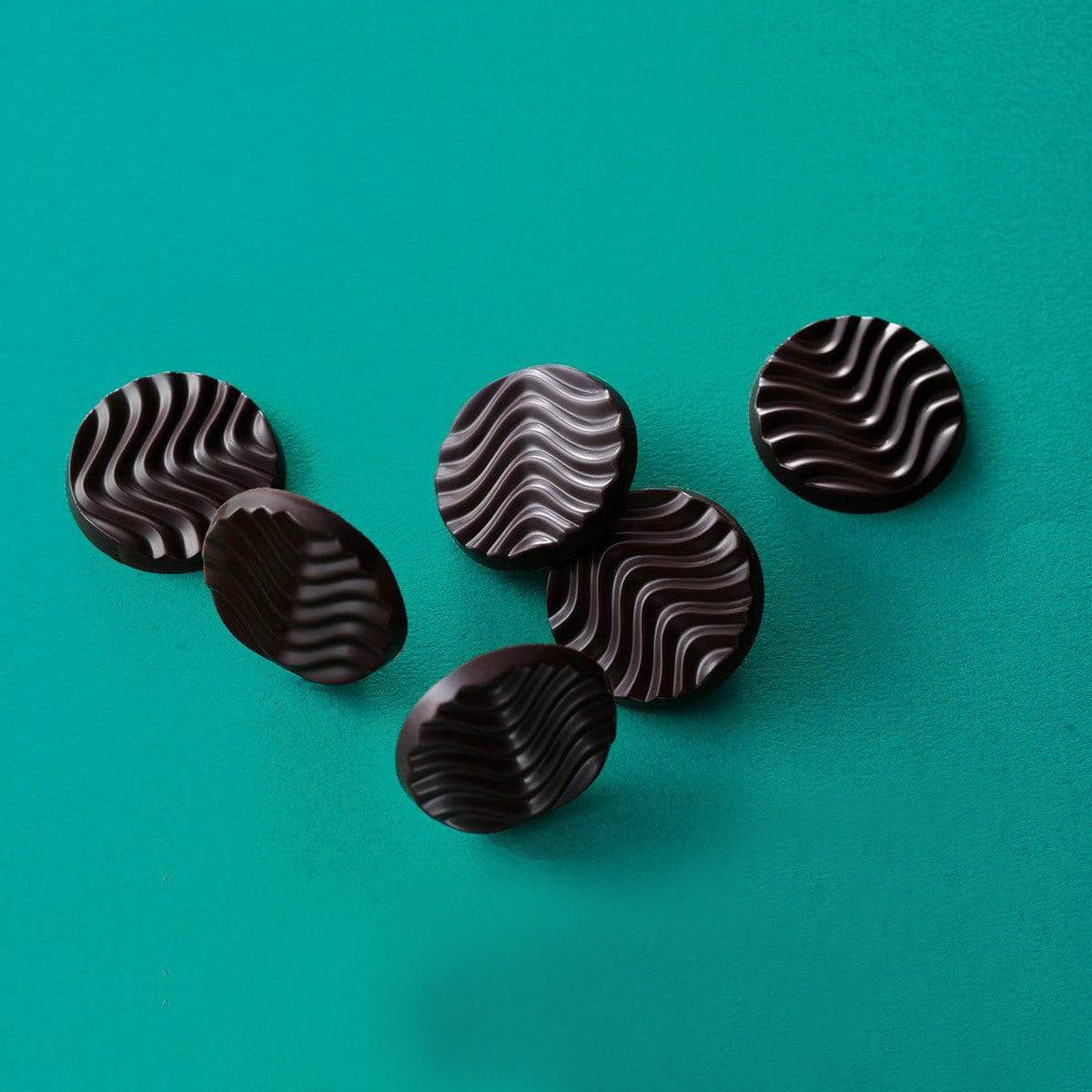 ROYCE' Chocolate - Pure Chocolate "Extra Bitter" - Image shows dark chocolate discs with a waved texture. Background and surface is in color blue-green.