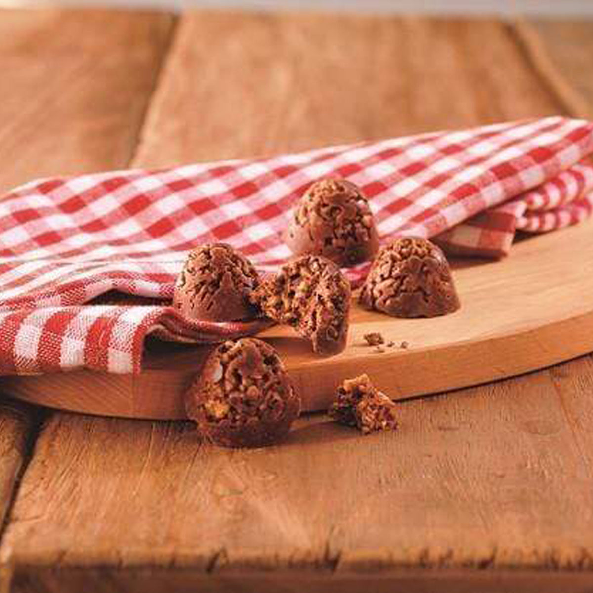 ROYCE' Chocolate - Potechi Crunch Chocolate - Image shows brown chocolate creations filled with crumbled potato chips, cornflakes, and cookie bits inside. Accents include a wooden chopping board and a tablecloth with red and white checkers. Background is brown wood.