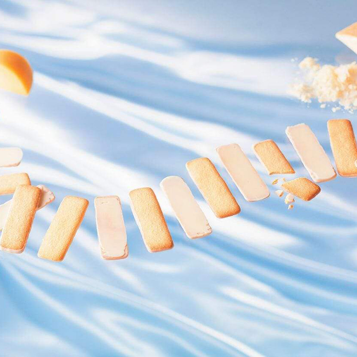 ROYCE' Chocolate - Baton Cookies "Fromage (25 Pcs)" -  Image shows golden cookies coated with white chocolate.  Accents include crumbs and blocks of yellow cheese. Background is in blue.