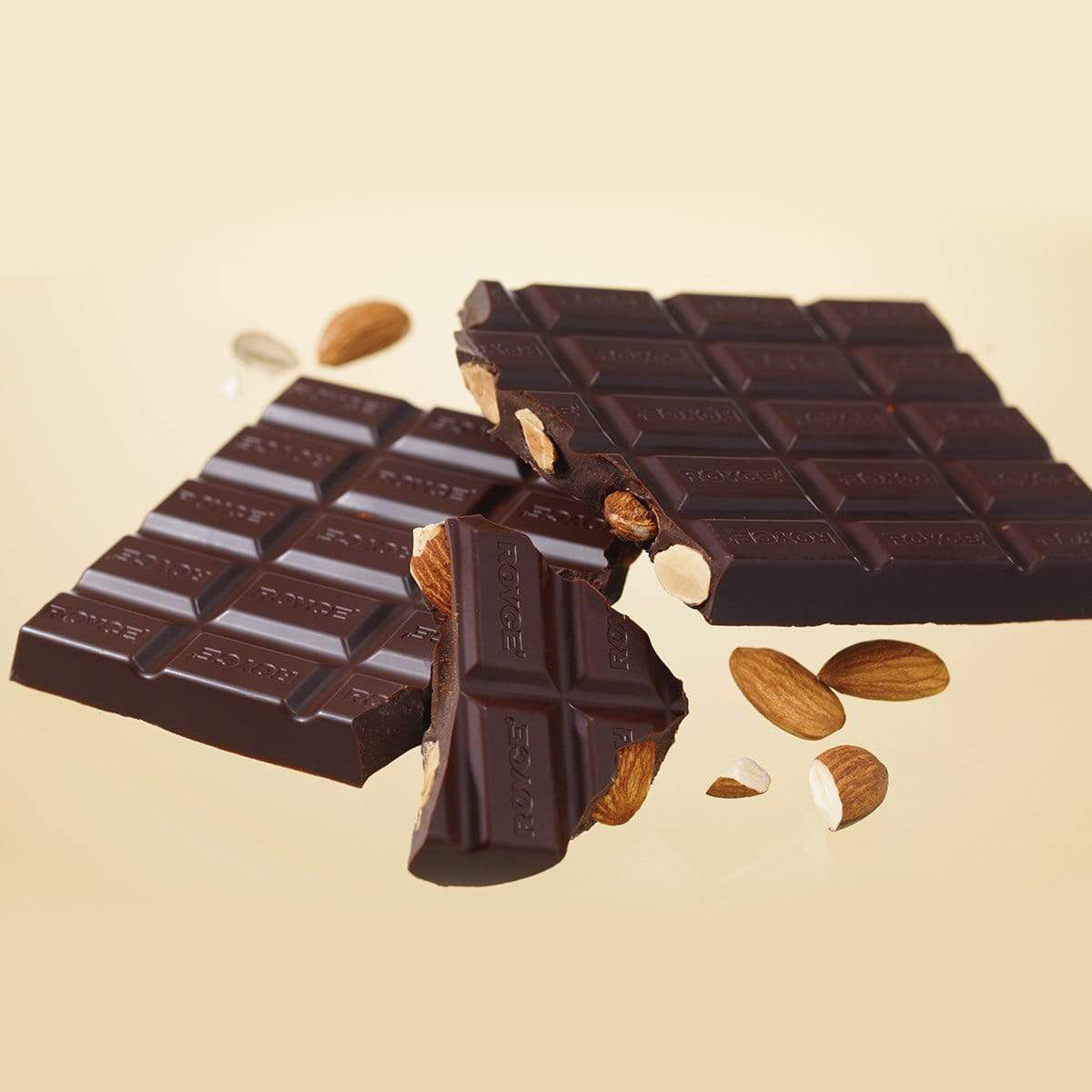 ROYCE' Chocolate - Chocolate Bar "Almond Bitter" - Image shows dark brown chocolate bars with with almonds and the word "ROYCE'" engraved. Background is in pale yellow with accents of almonds.