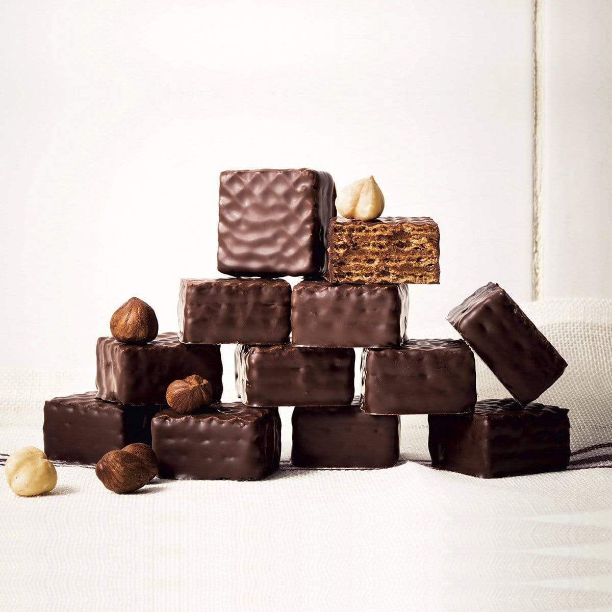 ROYCE' Chocolate - Chocolate Wafers "Hazel Cream" - Image shows stacks of brown chocolate wafers with accents of hazelnuts. Background is in white.