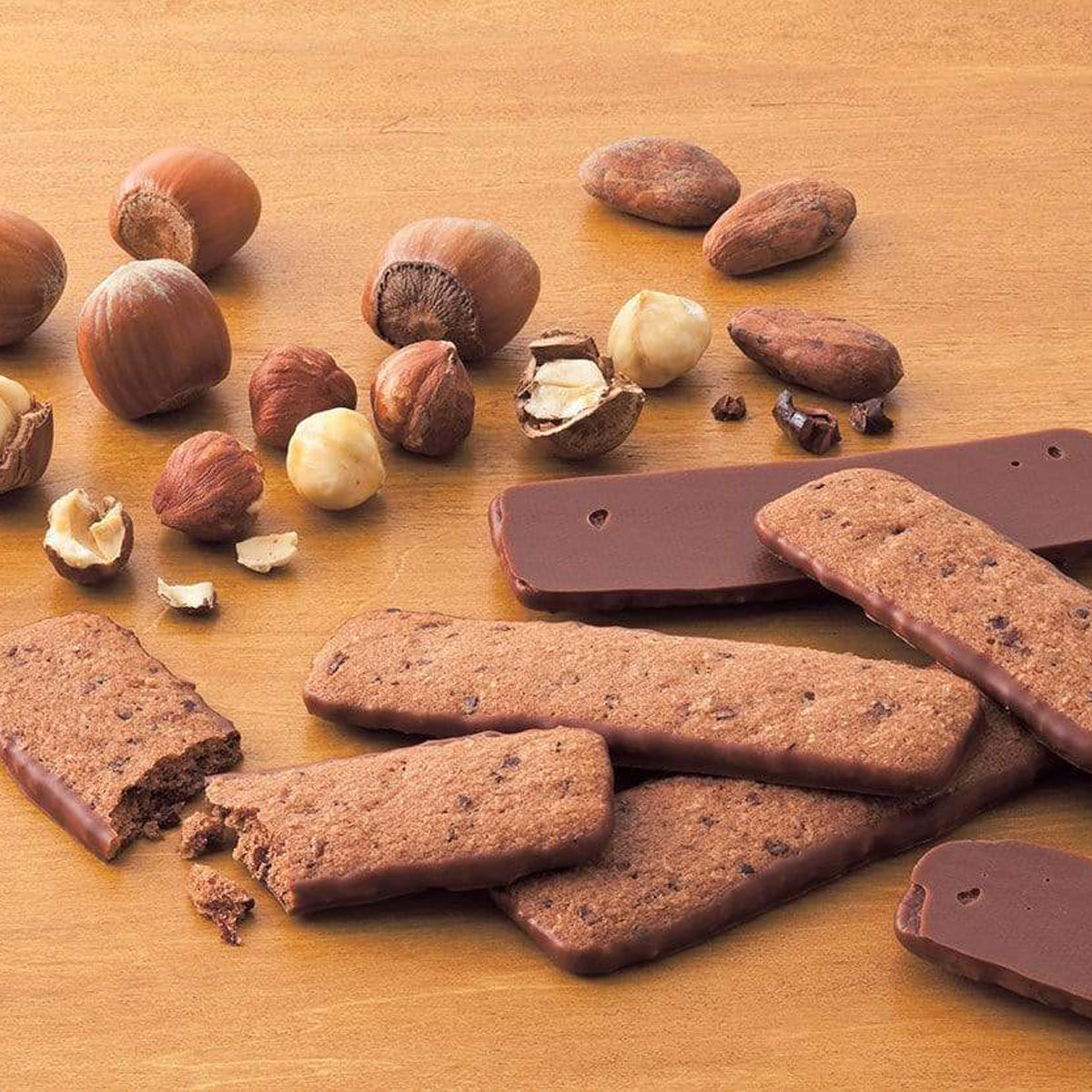 ROYCE' Chocolate - Baton Cookies "Hazel Cacao" - Image shows brown cookies with brown chocolate chips coated with brown chocolate. Accents include nuts in various shapes. Background is brown.