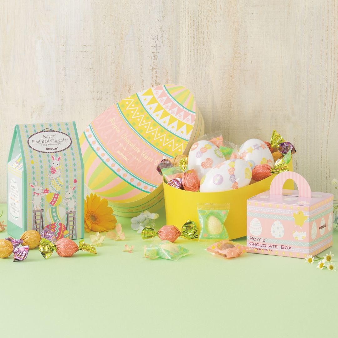 Pastel Easter display featuring Royce' chocolates: mint-green carton, egg-shaped box, yellow container with chocolates, small chocolate box, and scattered foil-wrapped candies.