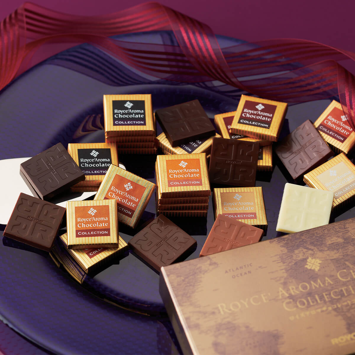 Assortment of Royce’ Aroma Chocolate Collection squares in dark, milk, and white chocolate on a platter, accompanied by the matching gift box and decorative ribbon.