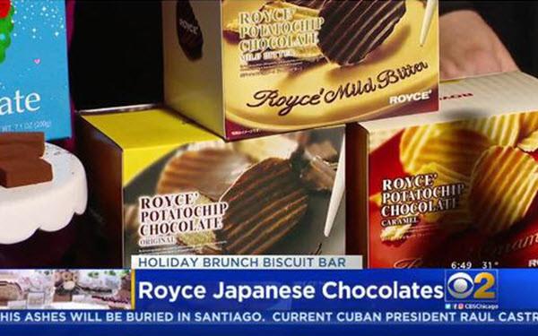 TV news clip showing boxes of Royce’ Japanese chocolates in Original, Caramel, and Mild Bitter flavors, with Holiday Brunch Biscuit Bar on-screen.
