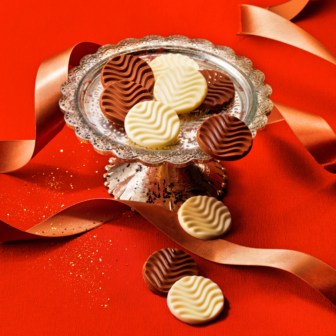 Image shows chocolate discs on a silver plate with gold ribbon. Background is in red.