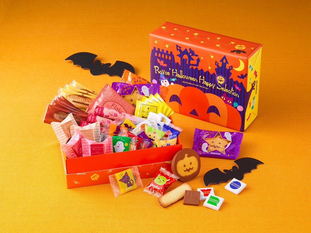 Halloween-themed gift box with assorted sweets: cookies, chocolate wafers, chocolates, pumpkin and star biscuits, candies in ghost and pumpkin wrappers, bat decorations.
