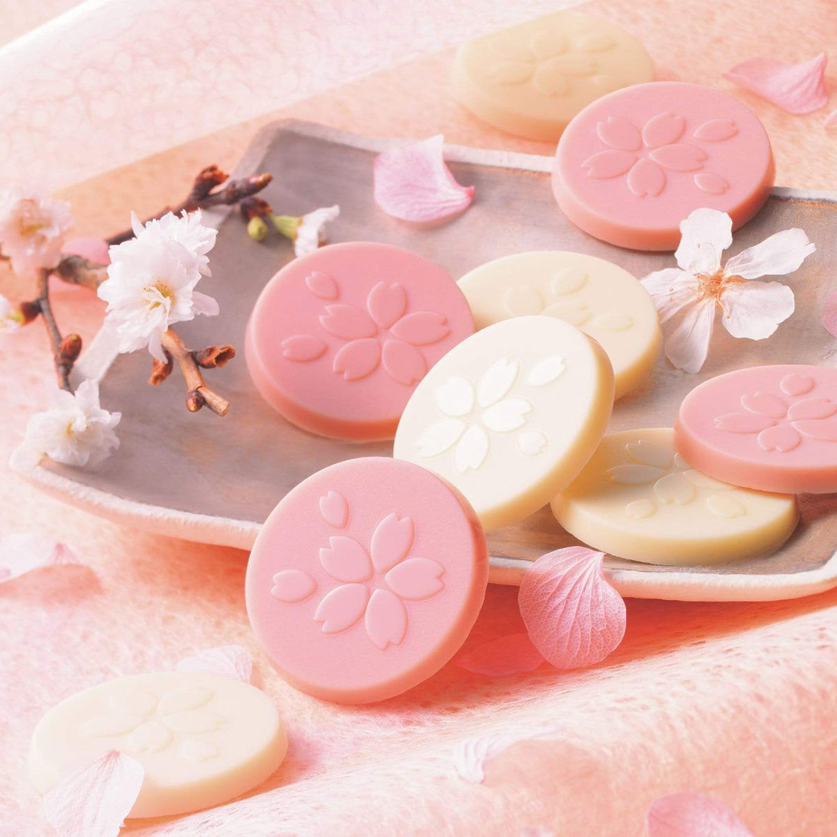 Image shows pink and white chocolate discs engraved with a flower pattern. Accents include loose flowers and a plate.