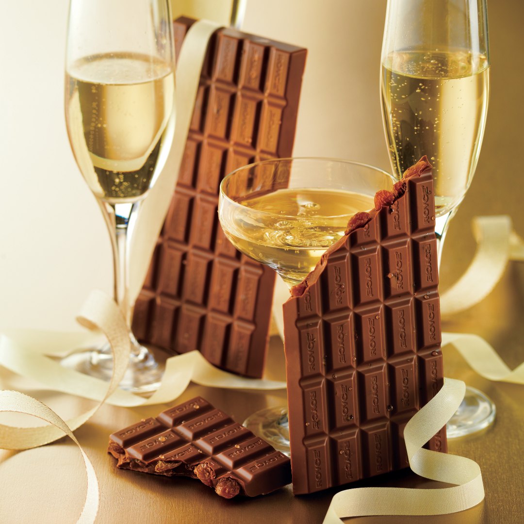 Image shows chocolate bars with gold ribbons and champagne glasses. Background is in gold.