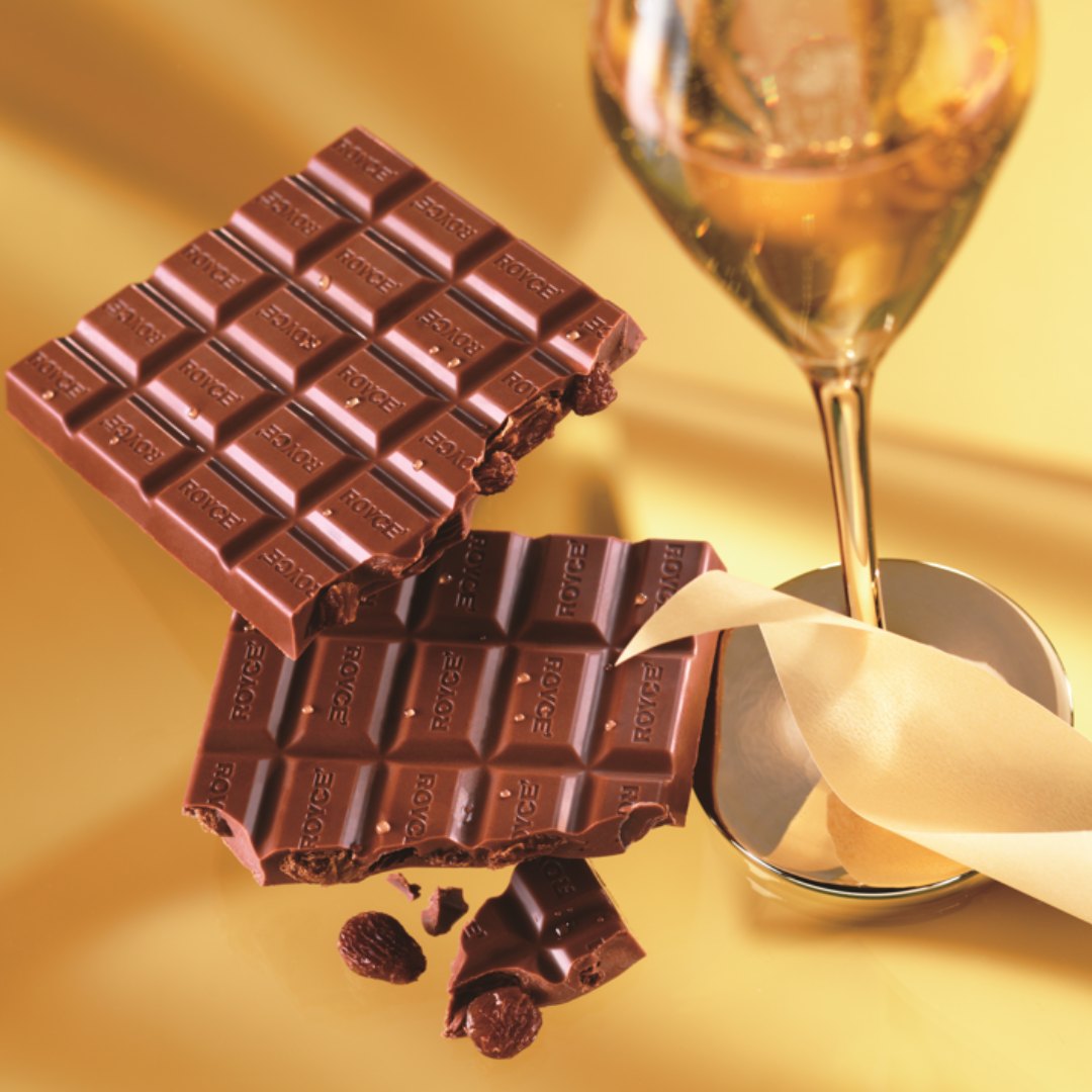 Image shows chocolate bars with gold ribbon and champagne glass. Background is in gold.