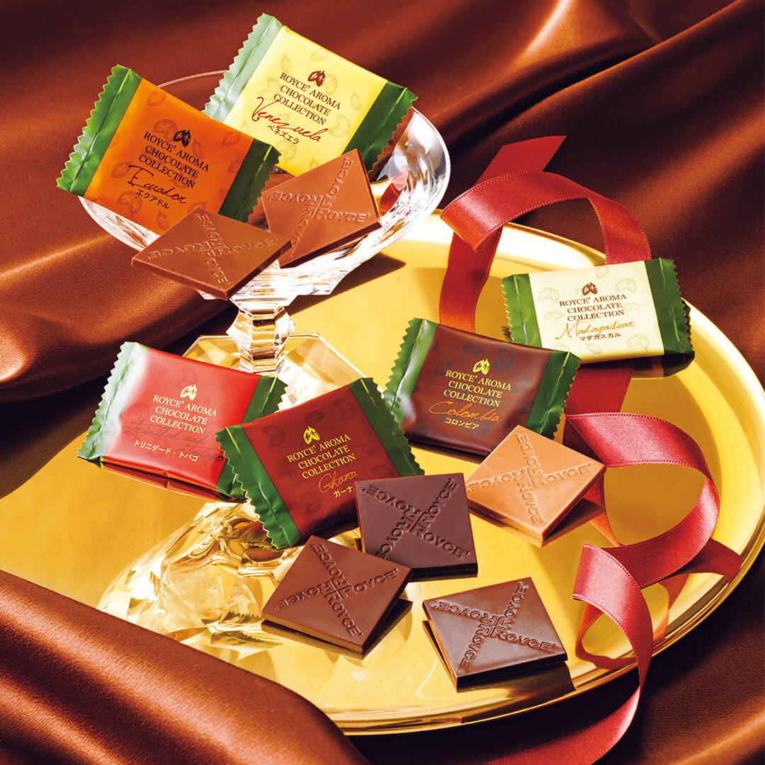 ROYCE' Chocolate - ROYCE' Aroma Chocolate Collection -  Image shows a individually-wrapped chocolate squares on a gold plate with glass. Accents include red silk and a red ribbon. 